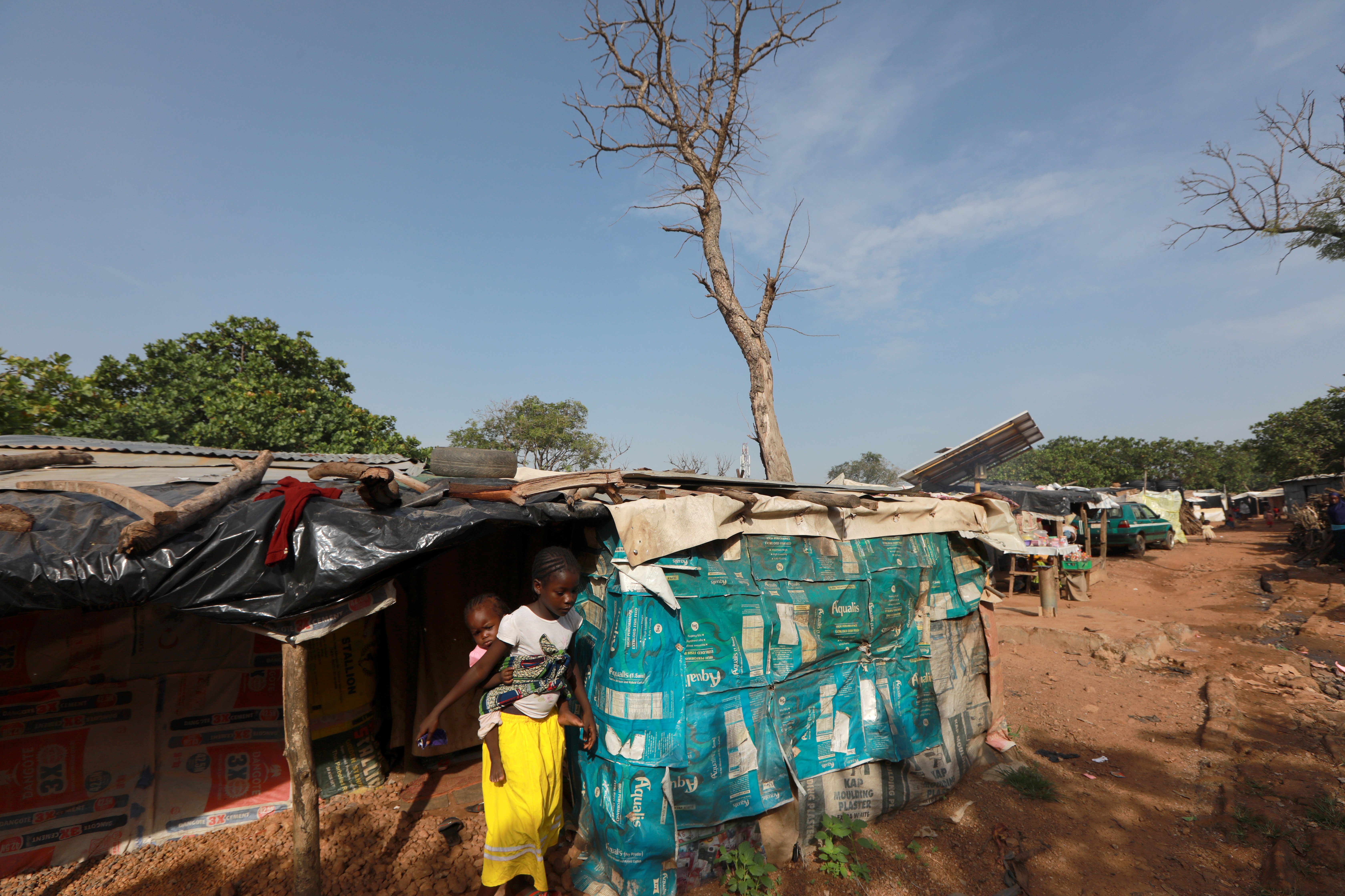 A hut in the New Kuchingoro refugee camp in Nigeria, with a young female walking out the door