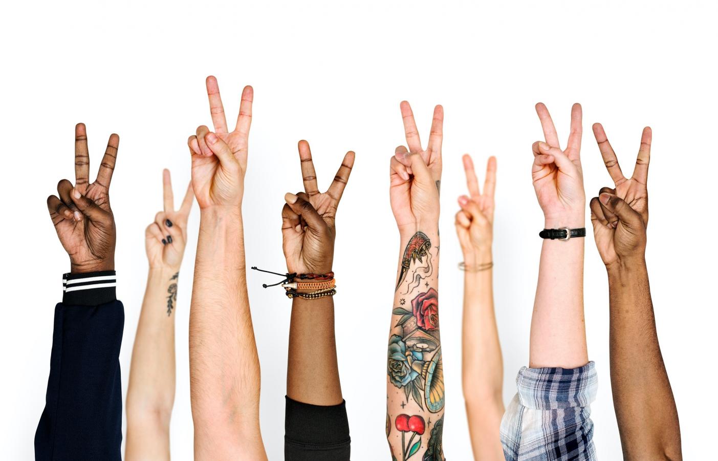 Hands of diverse ethnicities raised, each showing two fingered peace sign
