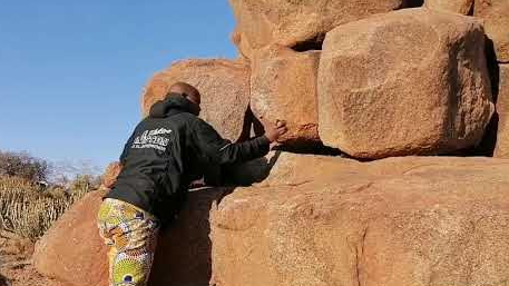 Volley Nchabeleng holds a small rock that he taps on the boulders to make music